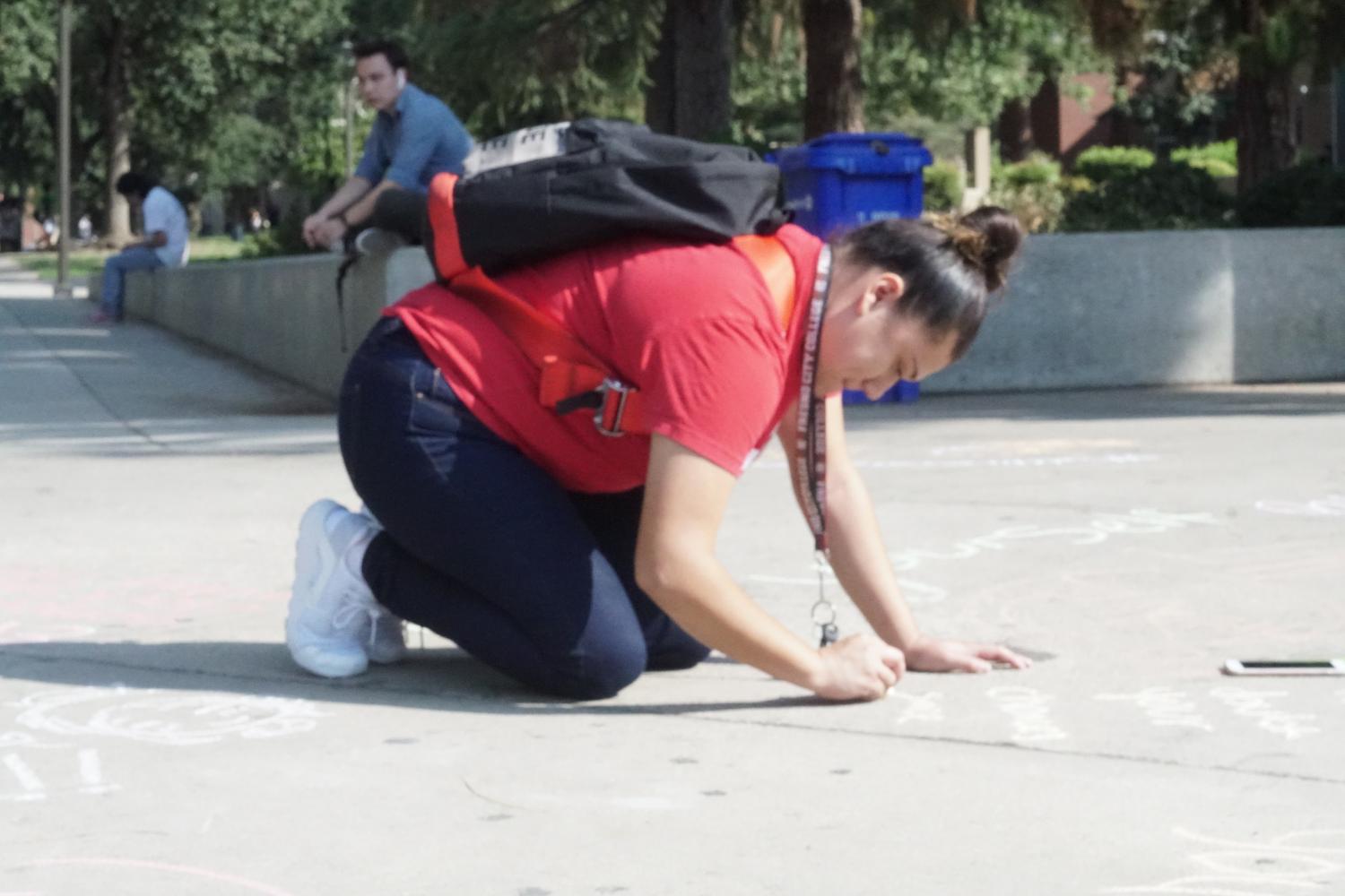 FCC student Diana Tearn writes an inspiring message near the main fountain at the Chalk It Out event for suicide awareness on Thursday, Sept. 7, 2017.