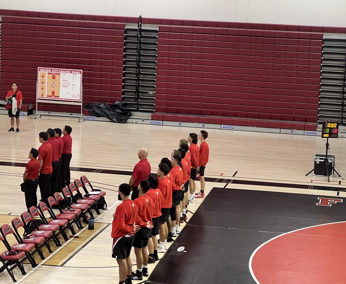 Fresno City Rams wrestlers and coaches stand up for the national anthem before the match at Fresno City College Gymnasium on Wednesday, Oct. 4, 2023.  