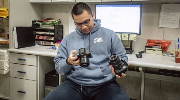 Staged photo of Jesus (Jesses) Herrera inspecting different cameras one is a Mirrorless [left] the other is a DSLR [Right] (Wednesday, November 11, 2023.
