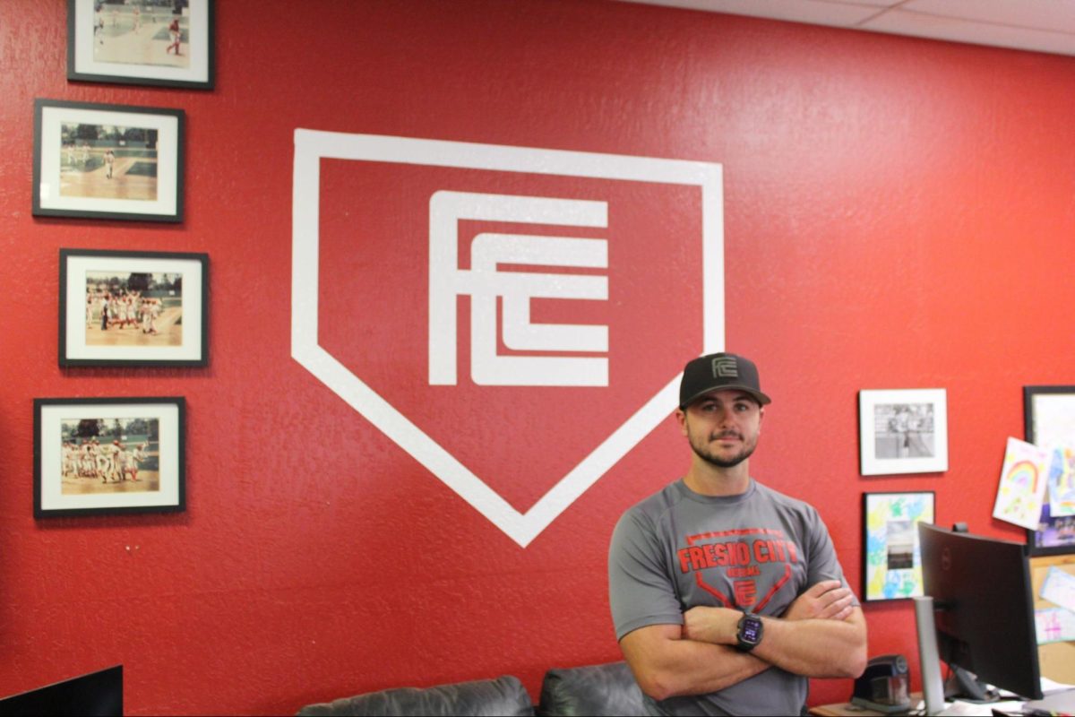 Fresno City College's Baseball Head Coach Mitch Karraker poses for photo in front of the Fresno City College logo and the team's awards on Sept. 2, 2025. 