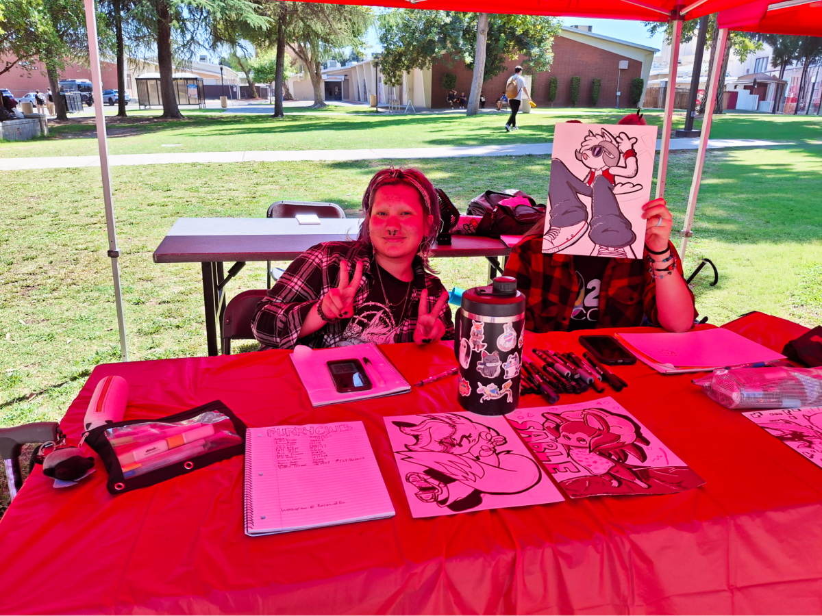 Lu Colmenero, president of the Furries of Fresno City College, holds up a peace sign at their Club Rush booth while C’Jay Pacheco, Inter-Club Council Representative and Social Media Manager, covers his face with art of Sammy the Rammy, the club mascot, on Aug. 27.