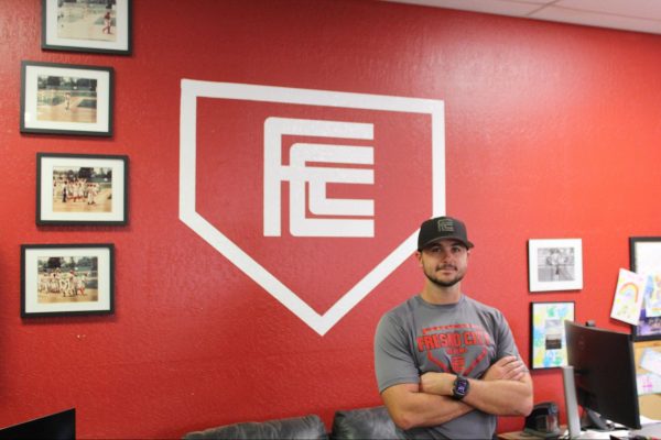 Fresno City College's Baseball Head Coach Mitch Karraker poses for photo in front of the Fresno City College logo and the team's awards on Sept. 2, 2025. 