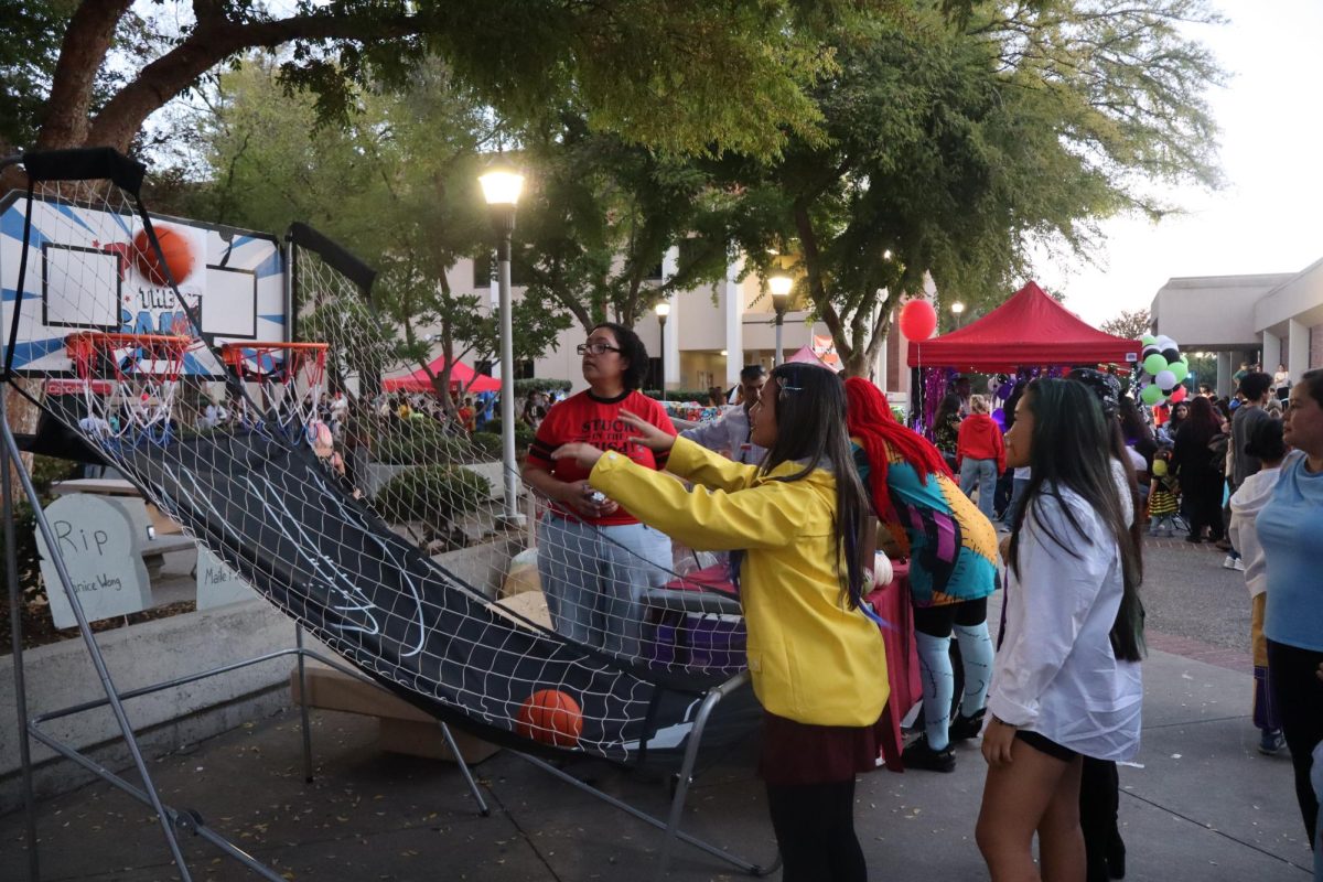 Carnival-goers play a basketball carnival game near a club's booth.