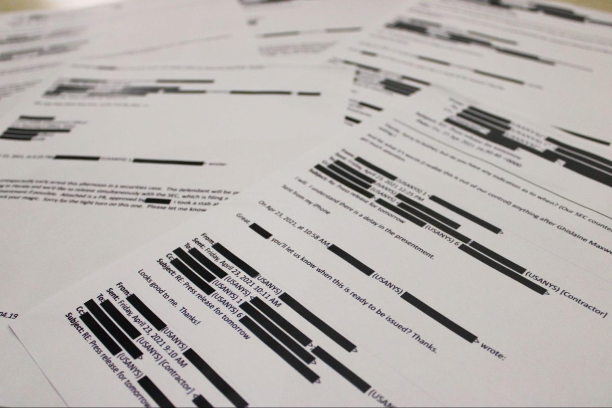 Photo of documents from the Epstein Files printed out with redacted text. 